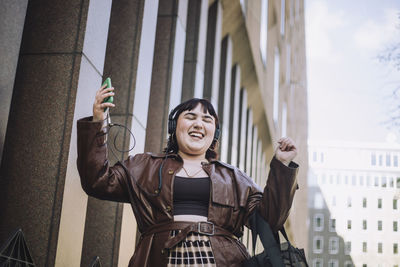 Happy young woman with eyes closed dancing while listening music through headphones