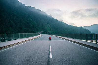 Mid distant view of man crouching on bridge towards mountain against sky