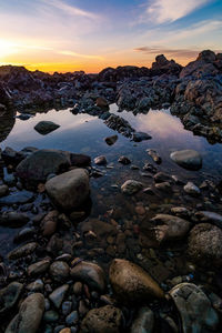 Pebbles on beach against sky during sunset
