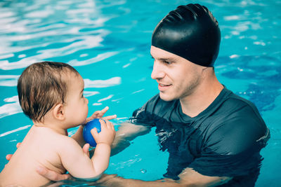 Father holding toddler son swimming in pool