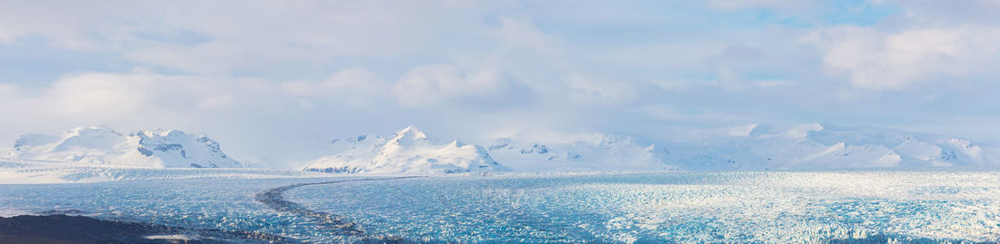 Panoramic view of snowcapped mountains by sea against sky