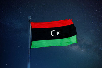 Low angle view of libyan flag against star field sky