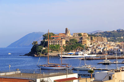 Sailboats moored on sea by buildings against clear sky