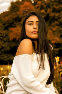 Portrait of beautiful young woman with long hair sitting against trees