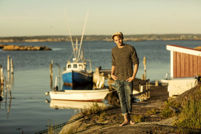 Full length of man standing with hands in pockets on rock formation at harbor