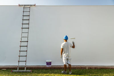 Unrecognizable young painter painting the facade of an apartment with a roller with the ladder on the side