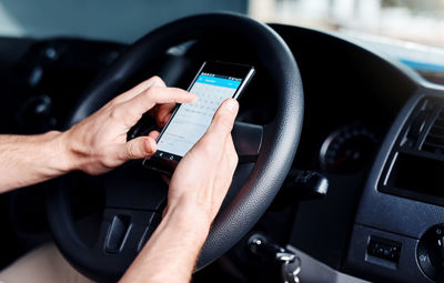 Cropped hand of man using mobile phone in car