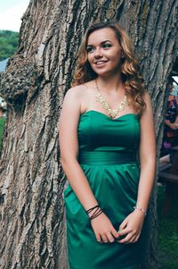 Young woman wearing green dress standing against tree trunk