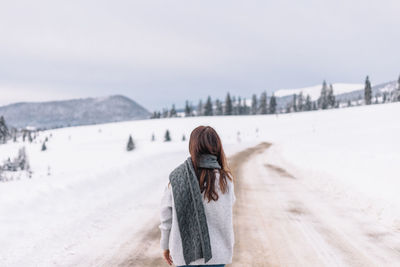 Woman walking on a road cover with snow while on a road trip in the mountains.