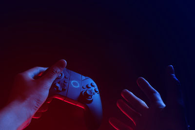 Close-up of hand holding game controller against black background