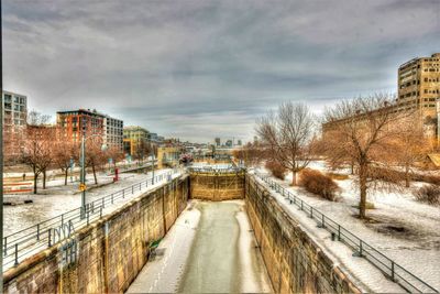 Snow covered road by buildings against sky