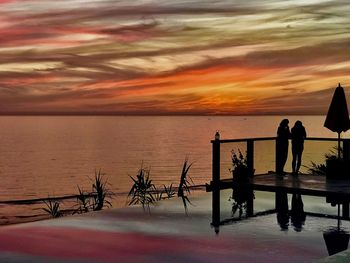 Silhouette people standing against railing during sunset