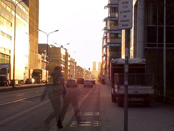 Vehicles on road in city against sky at sunset