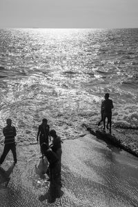Rear view of people standing on beach against sky