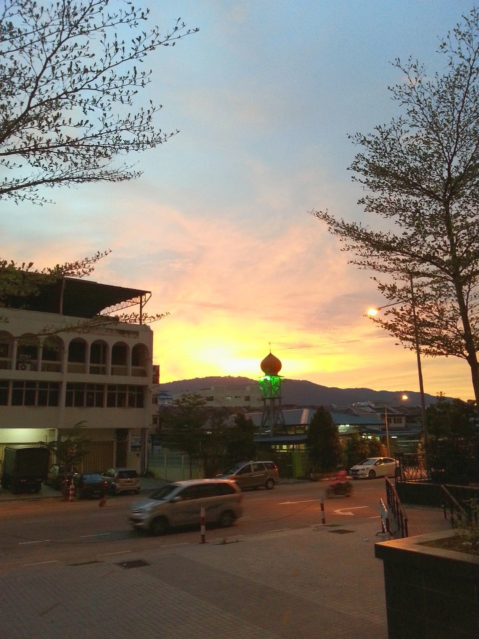 transportation, mode of transport, sunset, building exterior, sky, tree, architecture, built structure, car, land vehicle, bare tree, street, city, orange color, stationary, outdoors, cloud - sky, road, incidental people, branch