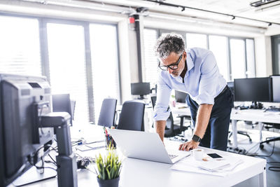 Mature businessman using laptop at desk in office