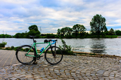 Bicycle on footpath by river against sky