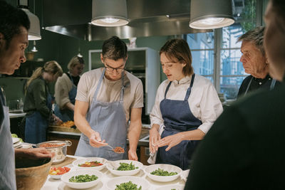 Female chef assisting male student during cooking class in kitchen