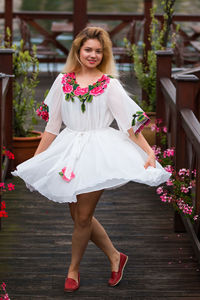 Portrait of smiling woman wearing white dress while standing on wooden footpath