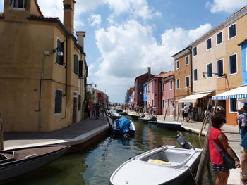 People on canal amidst buildings in city against sky