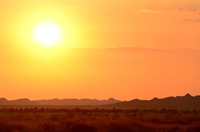 Scenic view of silhouette field against orange sky