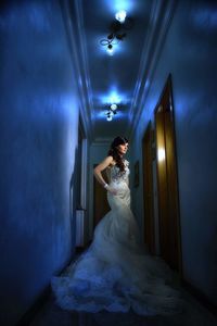 Portrait of young woman standing on illuminated corridor