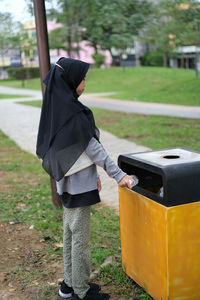 Rear view of woman throwing rubbish into the correct thrashbin