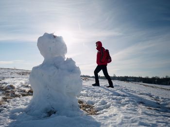 Man walk at icy snowman melting on last snowy place on spring hill. sunny spring day