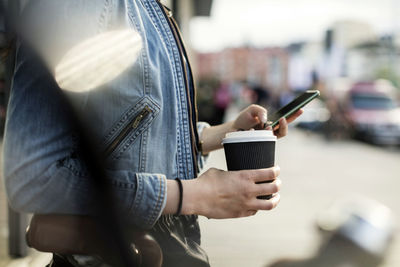 Midsection of woman holding smart phone and coffee cup in city