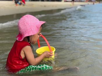 Girl playing with bucket while sitting at beach