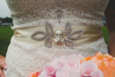 Midsection of bride standing with bouquet on field