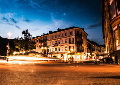 Illuminated street by buildings against sky at night