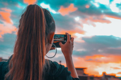 Rear view of woman photographing against sky during sunset