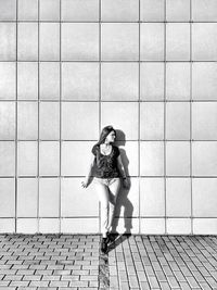 Full length of young woman standing against wall on sunny day