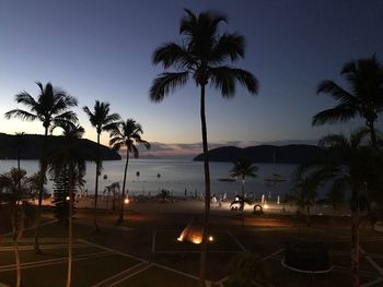 Silhouette palm trees by swimming pool against sky at sunset