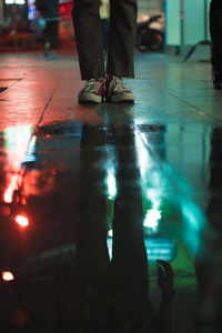 Low section of man standing by puddle on footpath