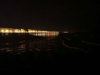 Illuminated city by river against sky at night