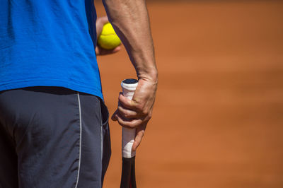 Midsection of player with ball and tennis racket on court