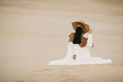 Muslim girl in hijab and niqab sitting on the beach sand dune