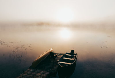 Empty dock with boats tied up on a foggy morning on a calm lake.