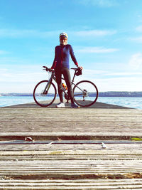 Woman standing with racing bike  by sea against sky