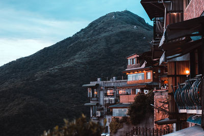 Buildings by mountain against sky at dusk