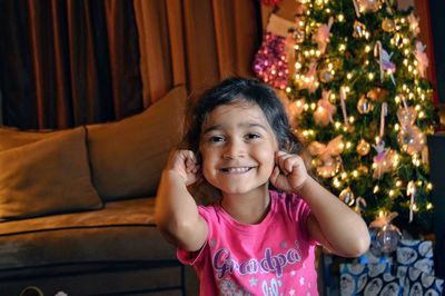 Portrait of smiling girl by christmas tree at home