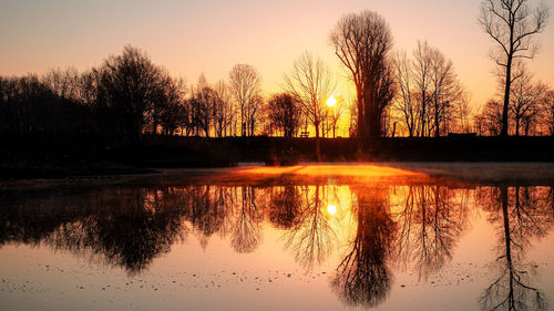 Silhouette trees by lake against sky during sunset