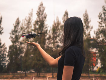 Rear view of woman gesturing towards drone against trees