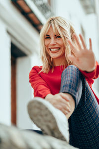 Portrait of smiling young woman waving hand in city