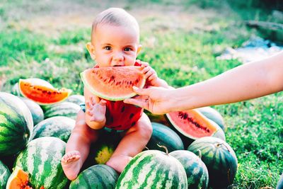 Woman giving watermelon slice to cute son at farm