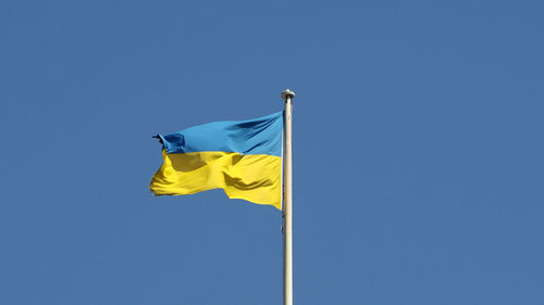 Low angle view of flag against clear blue sky