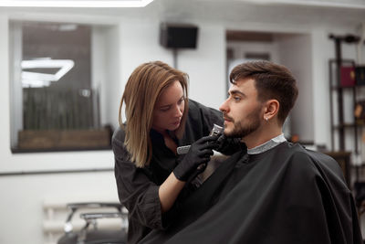 Woman shaving man beard in salon
