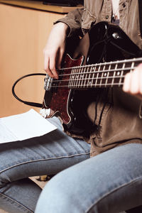 Crop view of a young woman playing elecrtic guitar. bass guitarist reading chords notes 